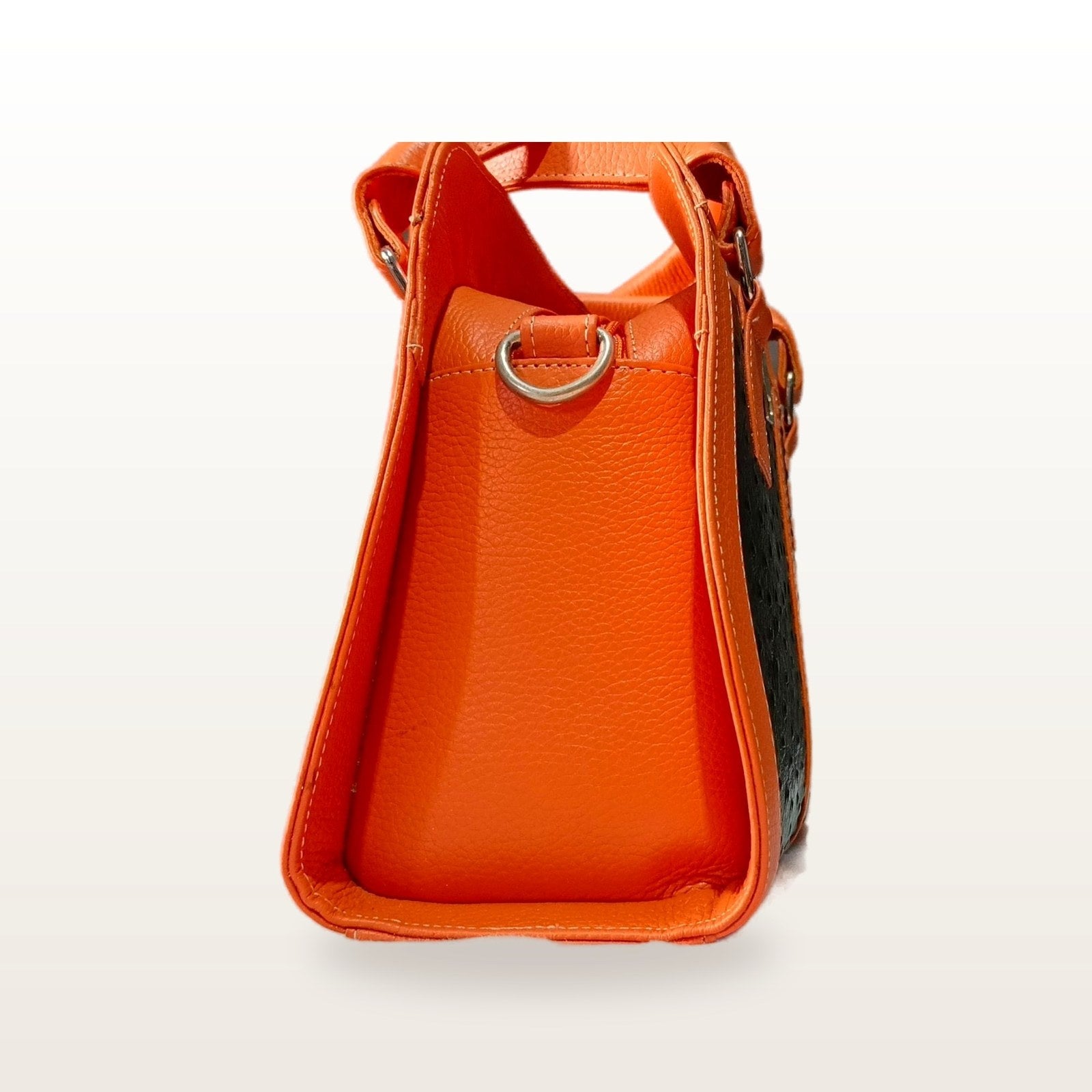 Side profile of the orange leather handbag, showing its depth and the strap ring