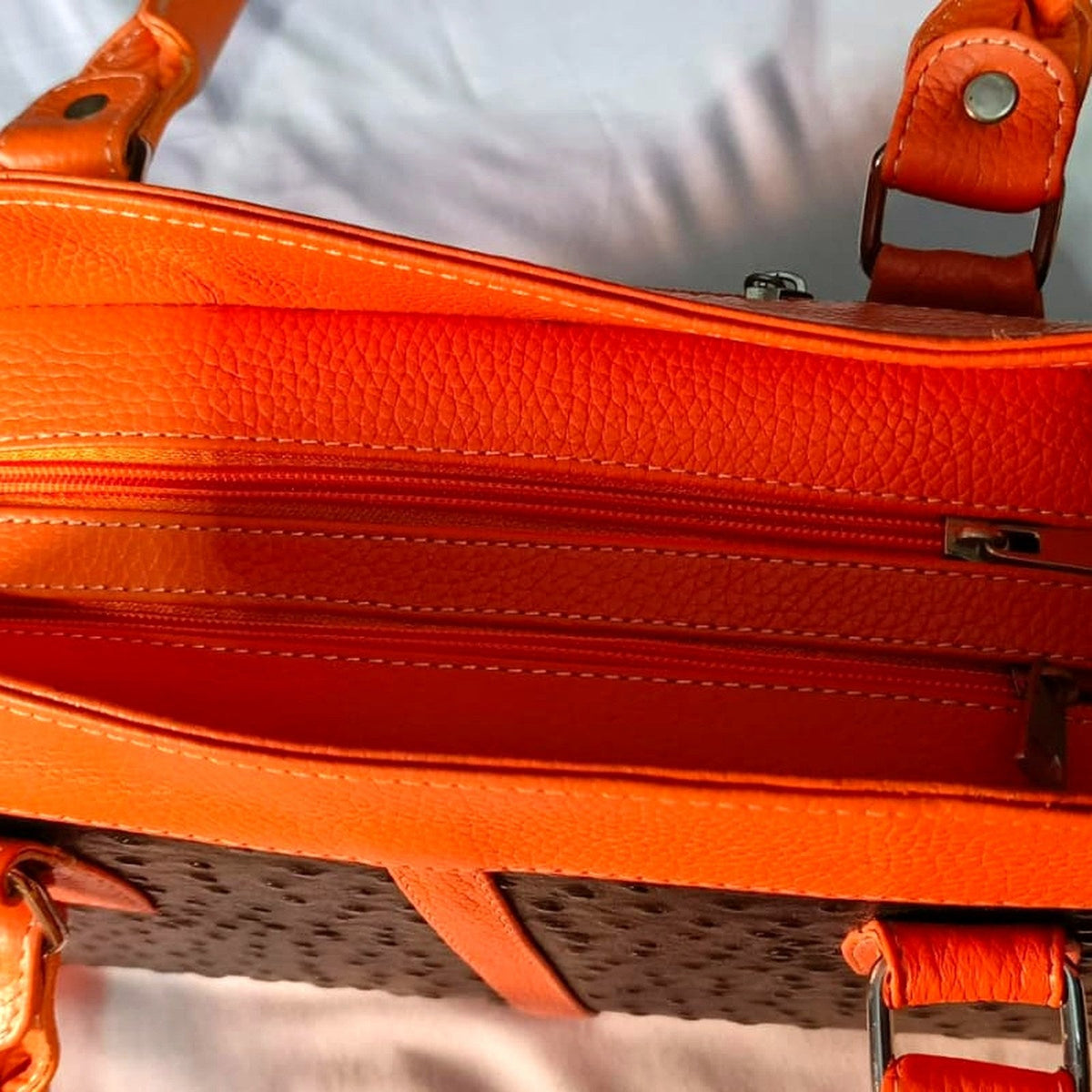 The handbag open from above, showing the three separate zipped compartments