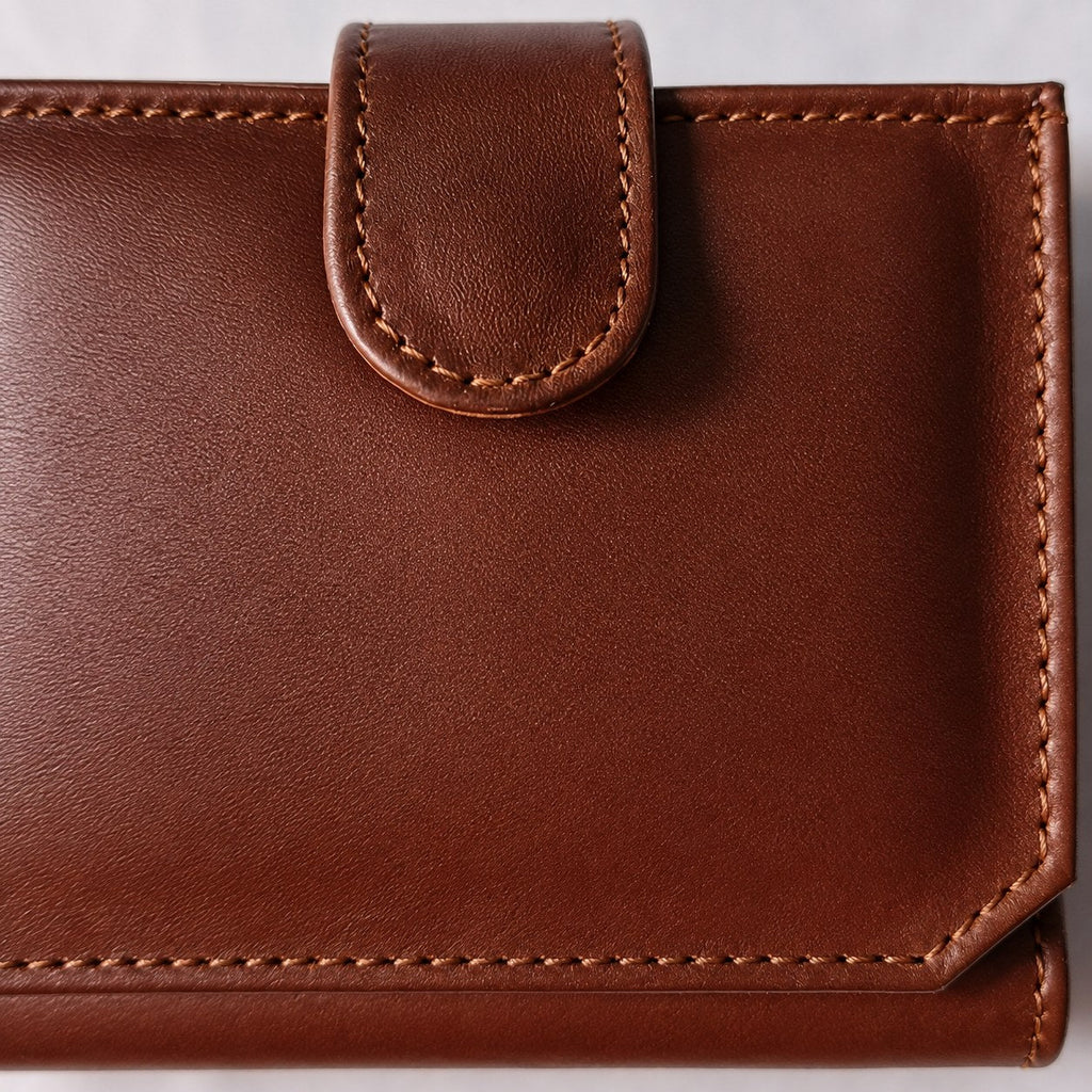 Close-up of the rounded leather closure tab and edge stitching on the brown flap wallet