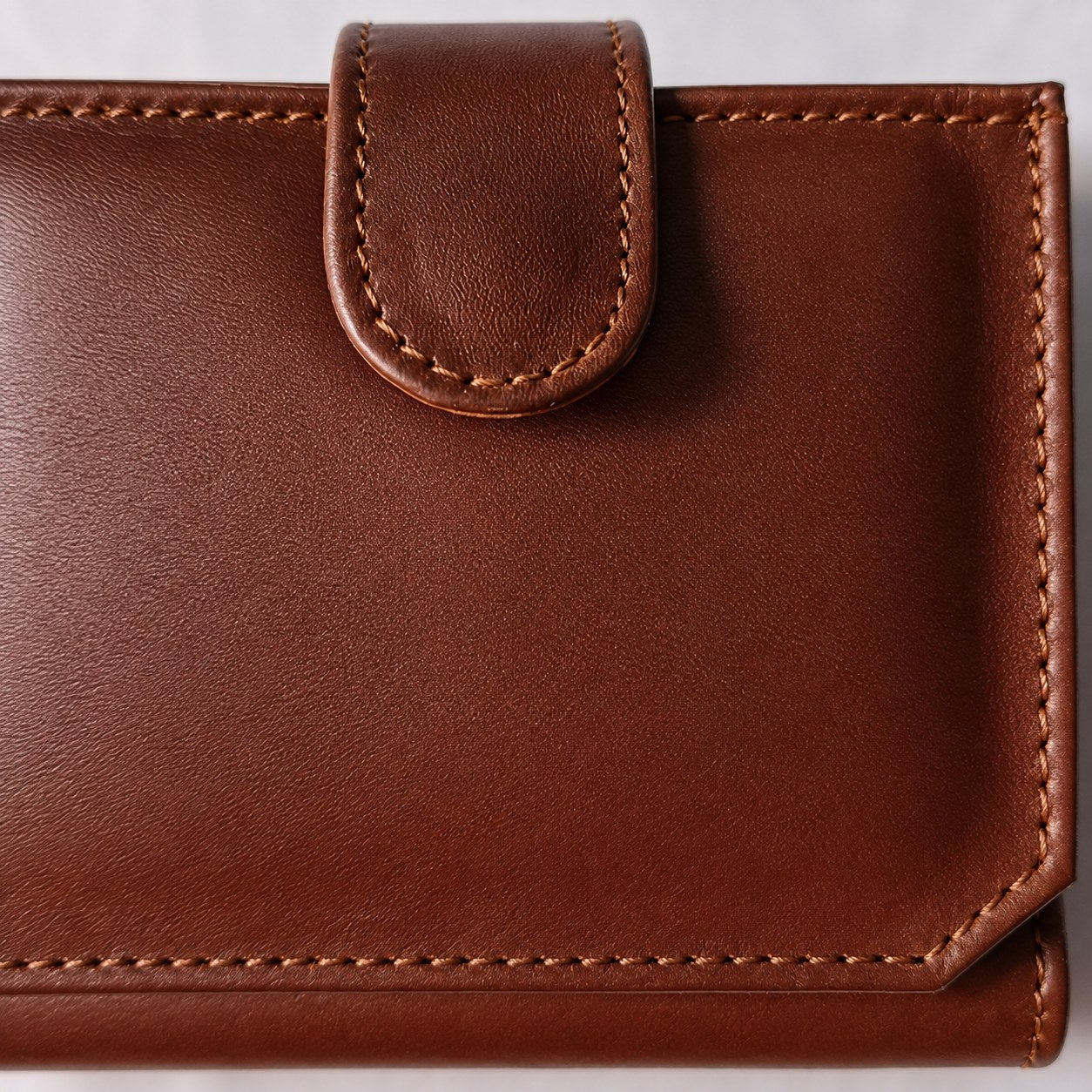 Close-up of the rounded leather closure tab and edge stitching on the brown flap wallet