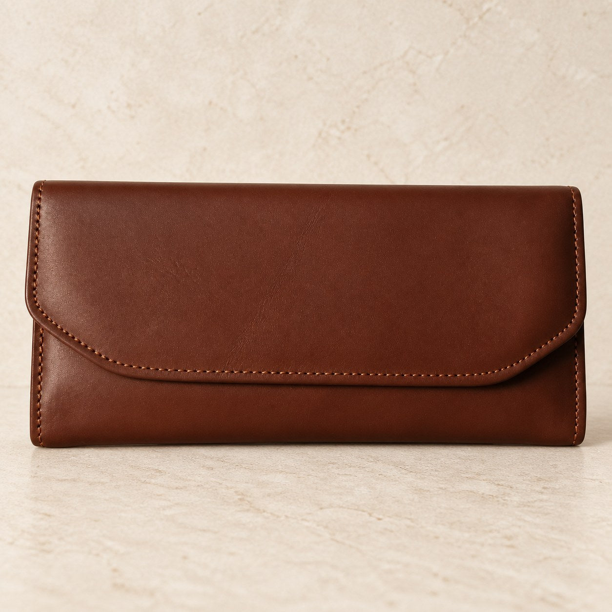 Brown leather envelope wallet photographed on a cream stone surface